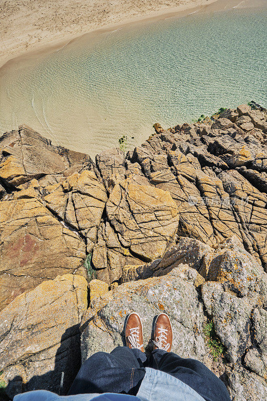 在Pedn Vounder海滩，康沃尔，POV向下看一个男人的腿和脚的悬崖边缘。